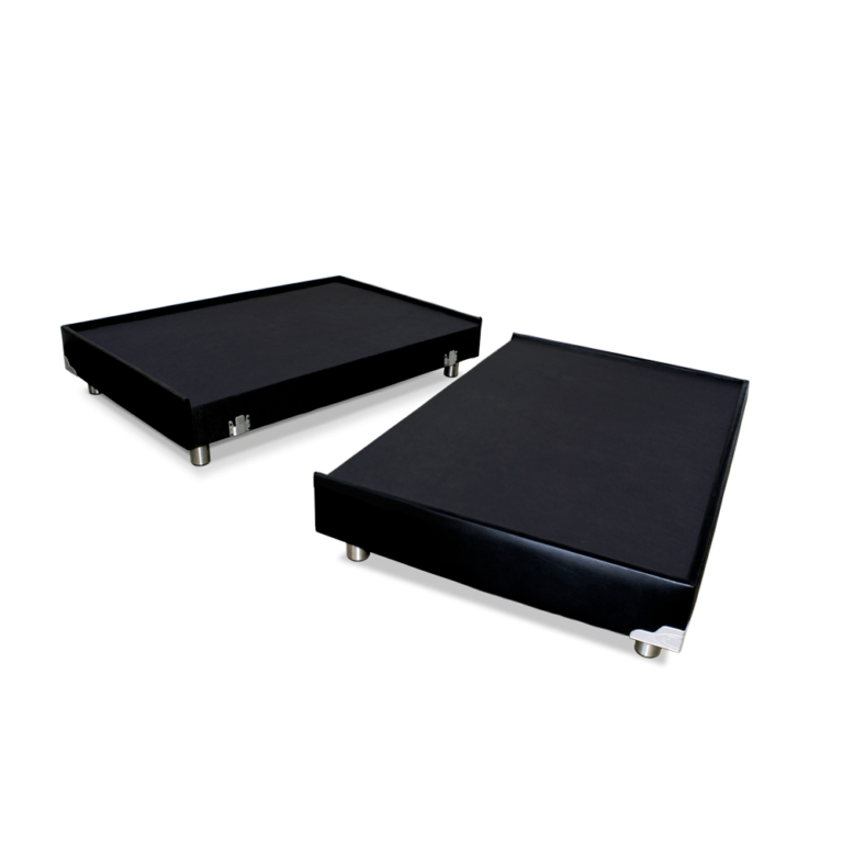 La imagen muestra dos base camas para colchón de tamaño estándar, ambas con un diseño moderno y elegante. Ambas bases están cubiertas en su totalidad por una tela negra, lo que les da un aspecto sofisticado. Cada base se apoya en patas metálicas plateadas, que proporcionan estabilidad y un toque contemporáneo. Las bases están diseñadas para poder conectarse entre sí mediante un sistema de anclaje visible en los laterales.