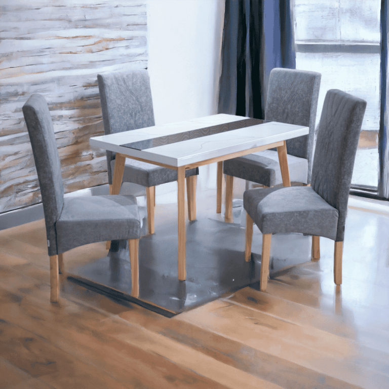 La imagen muestra un conjunto de comedor compuesto por una mesa rectangular y cuatro sillas. La mesa tiene una superficie blanca con un detalle decorativo en el centro y patas de madera clara. Las sillas están tapizadas en tela gris, con respaldos altos y patas de madera que combinan con las de la mesa.