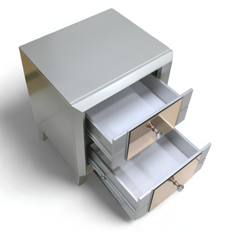 La imagen muestra un buró con un diseño moderno y lujoso. El buró está cubierto por completo con paneles de espejo que reflejan la luz y el entorno, dándole un aspecto brillante y elegante. Cuenta con dos cajones frontales, cada uno con un tirador en forma de cristal que añade un toque de sofisticación. El buró se apoya en cuatro patas ligeramente inclinadas hacia afuera, también cubiertas con paneles de espejo.