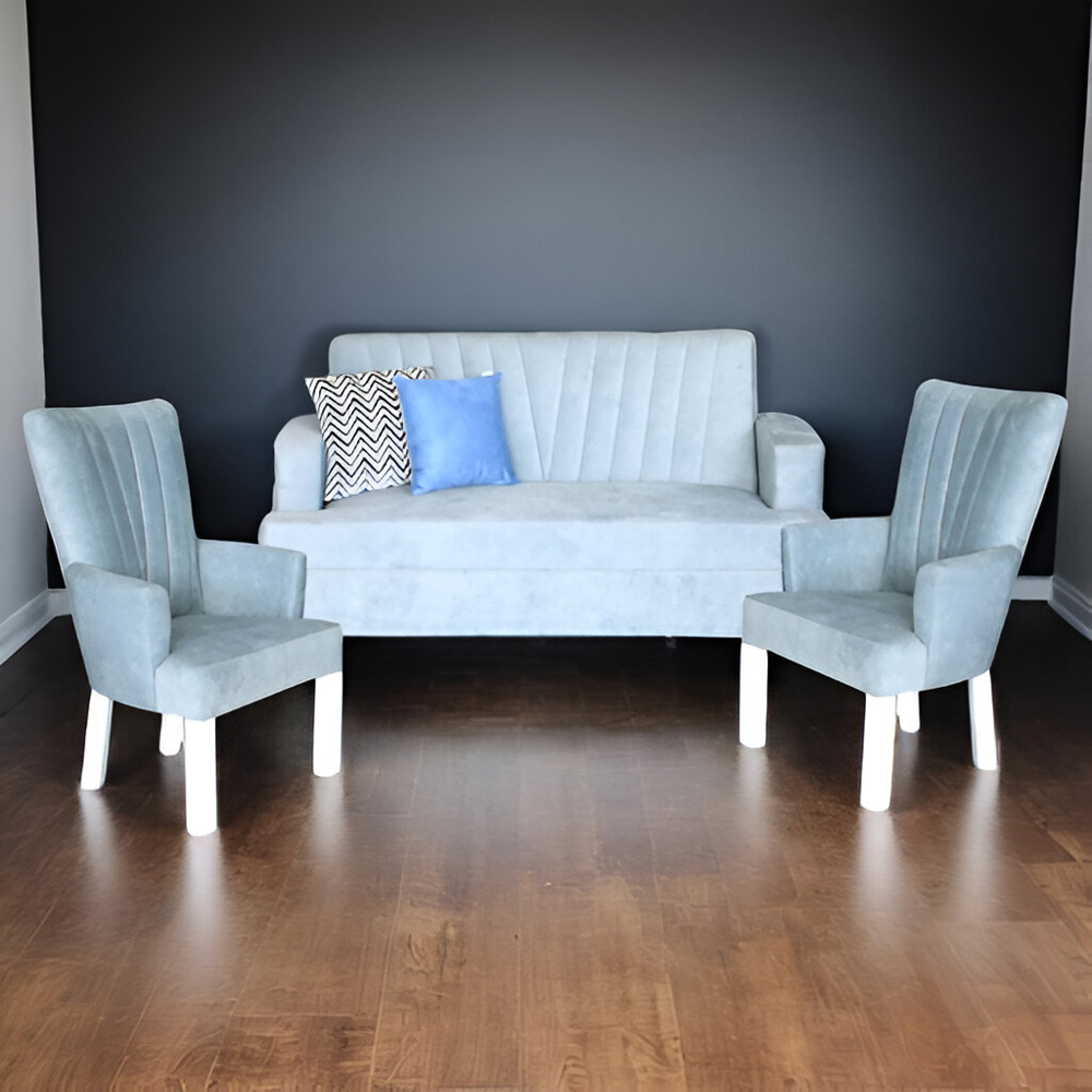 La imagen muestra un conjunto de sala compuesto por un sofá y dos sillones individuales, todos en color azul claro. El sofá tiene un diseño compacto con líneas verticales en el respaldo y dos cojines decorativos en tonos de azul y gris. Los sillones individuales presentan un diseño similar, con respaldos altos y patas blancas.